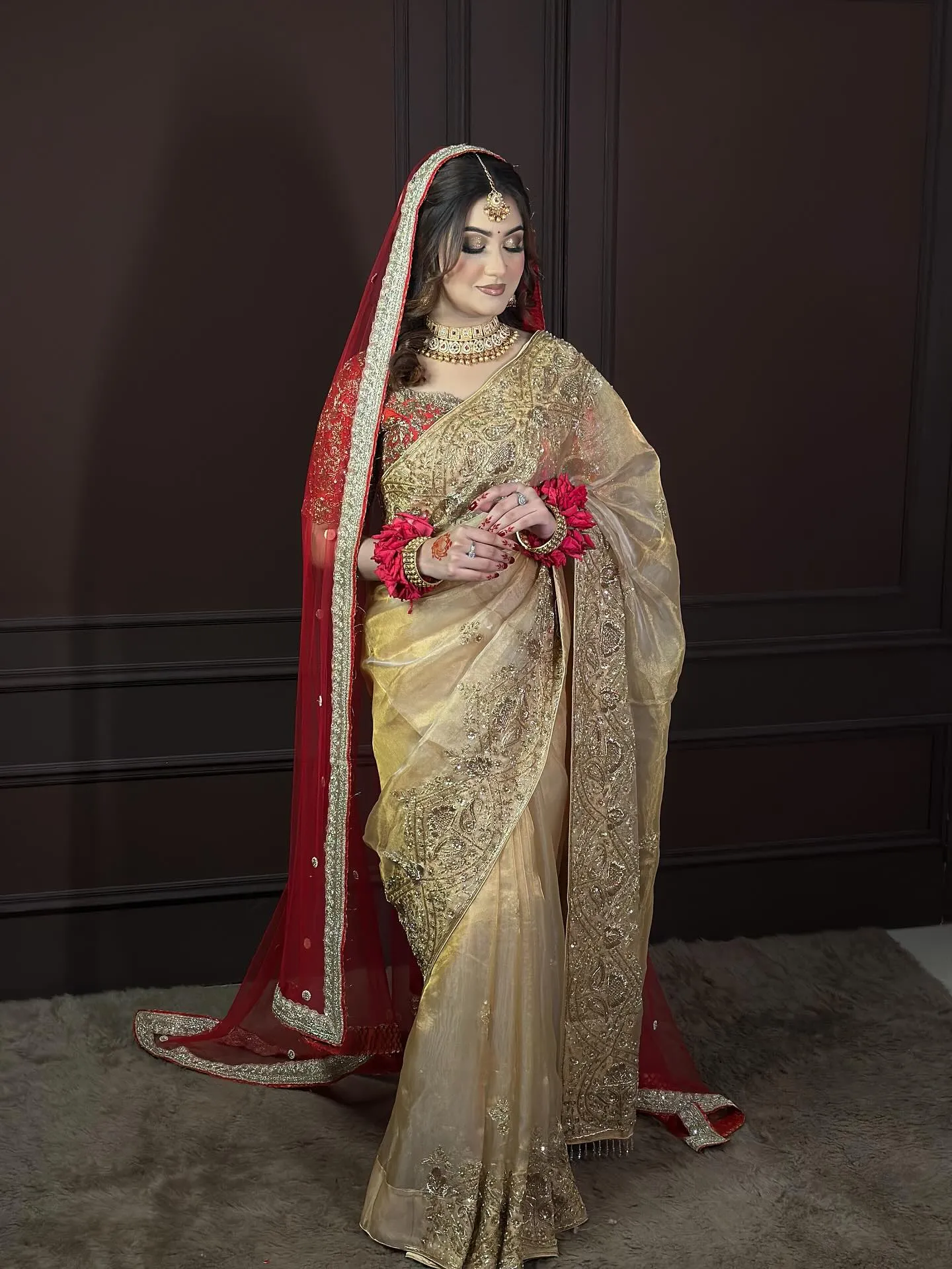 Bride in a gold saree with red veil, red blouse, floral bangles and gold choker, a karwa chauth look in saree