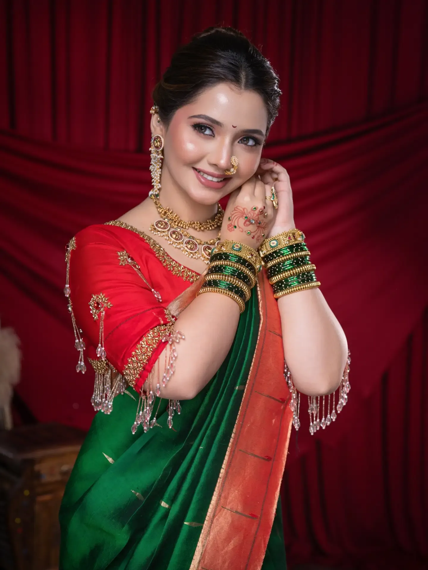 Woman in a green saree with orange border, red embroidered blouse, green and gold bangles and a nose ring