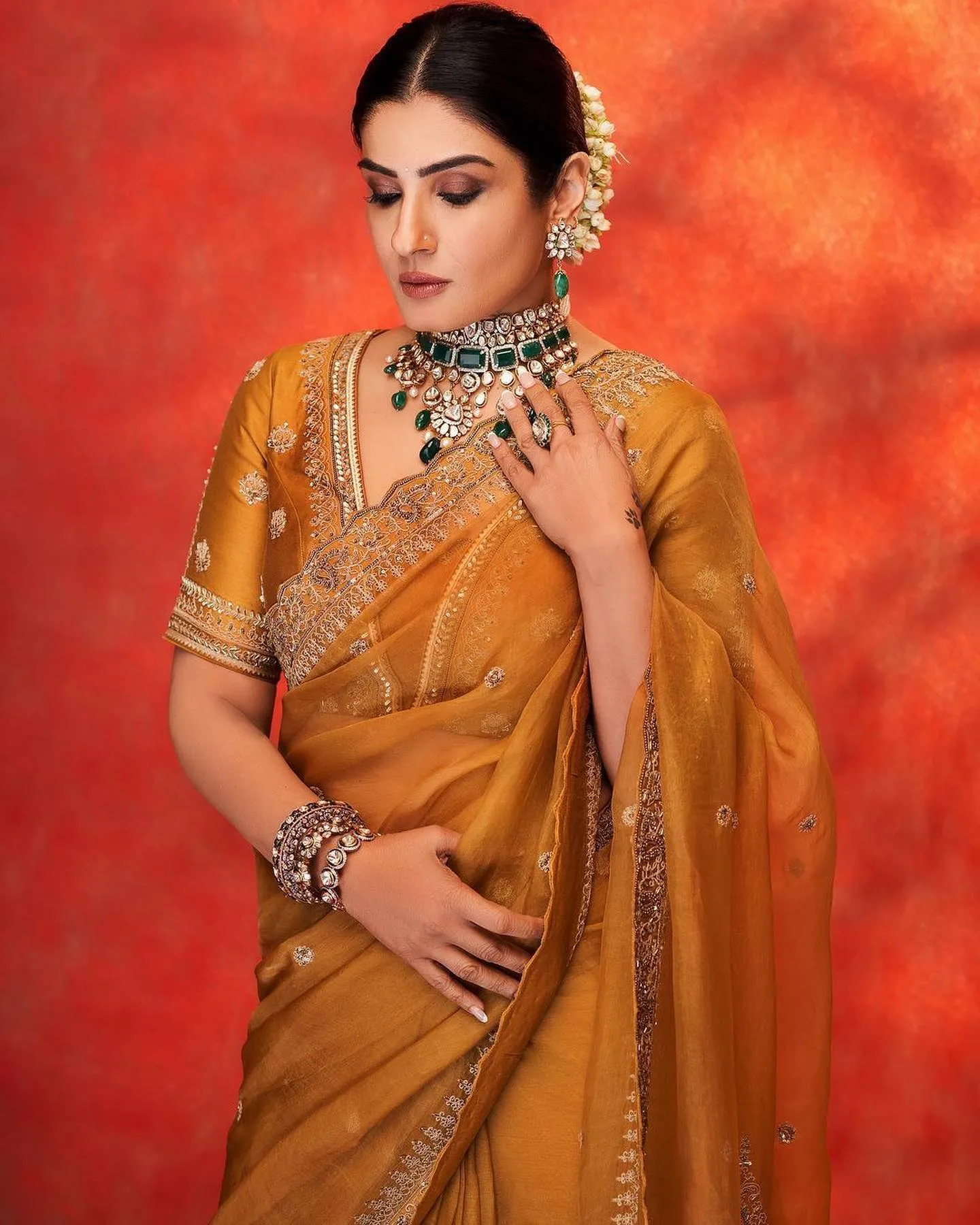 Woman in a mustard sheer saree with embroidered border, green choker and white flowers in a sleek bun