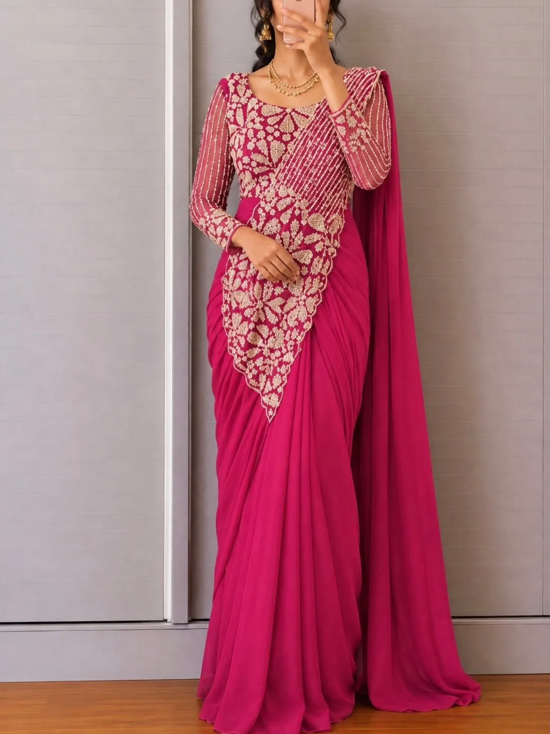 Woman in a magenta saree with gold embroidery, beaded sheer sleeves and a layered gold necklace