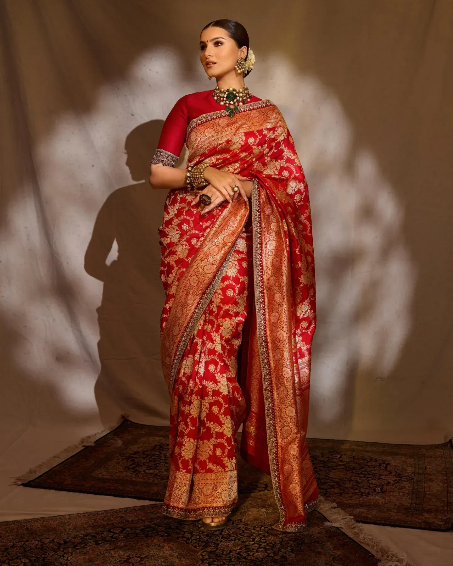 Woman in a red saree with gold floral weaving, green choker and flowers in a low bun